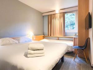 a hotel room with two beds and a desk and a window at ibis Rennes Cesson in Cesson-Sévigné