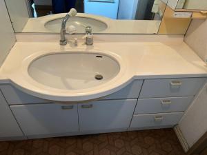 ein weißes Waschbecken in einem Badezimmer mit einem Spiegel in der Unterkunft Okegawa Quiet Homestay in Okegawa