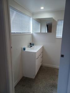 ein weißes Badezimmer mit einem Waschbecken und zwei Fenstern in der Unterkunft Cosy Cottage in Ruakaka