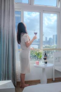 a woman holding a glass of wine in front of a window at Palmier Hotel - Art House Da Nang in Da Nang
