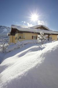 a house covered in snow with the sun in the background at Hotel Hubertus in Brixen im Thale