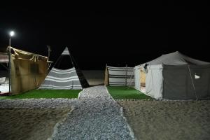 een groep tenten in een veld 's nachts bij Sanmar camp in Ḑibāb