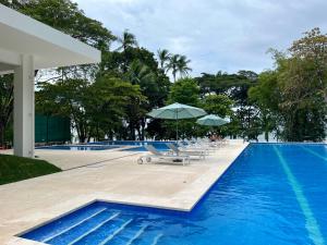a swimming pool with chairs and umbrellas next to it at Modern Beach Apartment - Walk to Playa Mantas & Beach Club Access in Punta Leona