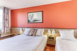 zwei Betten in einem Zimmer mit einer orangefarbenen Wand in der Unterkunft Ace Hotel Montluçon in Saint-Victor