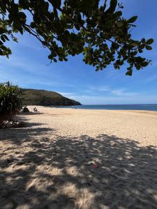 a view of a sandy beach with a tree overhead at Suites e Casa_Pauba in São Sebastião