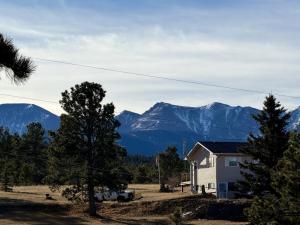 une maison dans un champ avec des montagnes en arrière-plan dans l'établissement Cozy Rustic Retreat on a Horse Ranch with Stunning Pikes Peak Views and Serenity Minutes from Downtown Woodland Park, à Woodland Park