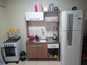 a small kitchen with a refrigerator and a sink at Apart próximo a Unimed, Catedral e HSA com 2 quartos com 2 ARES e garagem in Santo Ângelo