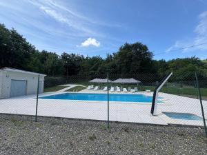 a fence surrounds a swimming pool with chairs and umbrellas at Albizias 3 in Eugénie-les-Bains