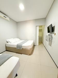 a white bedroom with a bed and a flat screen tv at Pousada Cidade Nova in Campo Maior