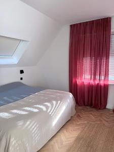 een slaapkamer met een bed en een raam met rode gordijnen bij Maison de L'Histoire - Fleur de Pivoine in Sint-Martens-Latem