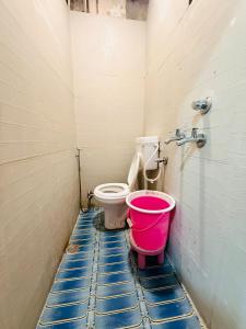 a bathroom with a toilet and a pink bucket at Hotel Tathastu Inn in Ujjain