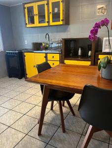 a kitchen with a wooden table and yellow cabinets at Casa no Centrinho para 2 pessoas 100m do Mar in Bombinhas