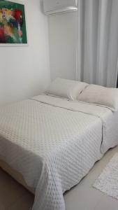 ein Bett mit weißer Bettwäsche und einem Bild an der Wand in der Unterkunft Solaris Residencial Clube in Ilhéus