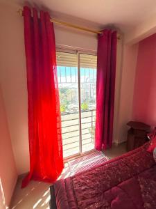 een slaapkamer met rode gordijnen en een groot raam bij Face à la Mer TANGER in Hauara