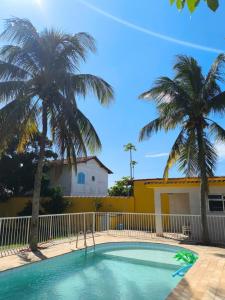 a swimming pool with palm trees in front of a house at Casinha Guest House in Saquarema
