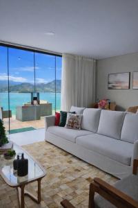 ein Wohnzimmer mit einem weißen Sofa und großen Fenstern in der Unterkunft Maravilhosa casa linear 5 suítes em Angra in Angra dos Reis
