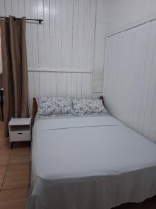 a white bed in a room with a white wall at Kitnet Avenida in Imbituba