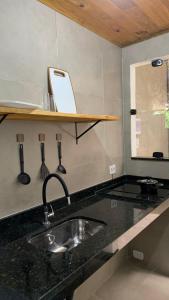 a kitchen counter with a sink and a shelf with utensils at Embaúba Paraty - Hostel & Flats in Paraty