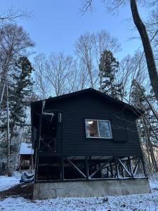 a black cabin in the woods in the snow at Pebble Mountain Cabin in Shinano