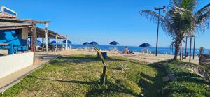 a beach with a building and a palm tree and the ocean at Flat Saigon Barra de Maricá Pé na Areia Wi-Fi in Maricá