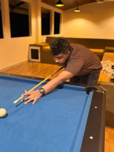 un homme penché sur une table de billard avec des queues de billard dans l'établissement Ceylon Lodge - Airport Transit Hostel, à Negombo