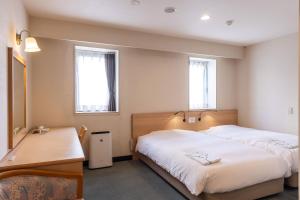 a bedroom with two beds and a desk and two windows at Ace Inn Matsumoto in Matsumoto