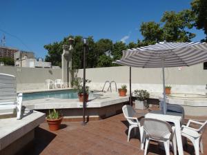 um pátio com um guarda-sol e cadeiras e uma piscina em Altezza Apart Suites em Mendoza