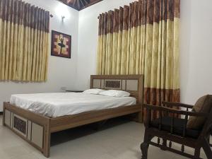 a bedroom with a bed and a chair and curtains at Naturus Villa Thalpitiya in Panadura
