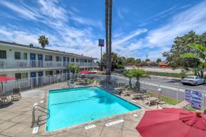 a pool with chairs and umbrellas next to a hotel at Motel 6-Westminster, CA - South - Long Beach Area in Westminster
