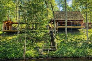 a tree house in the woods with a staircase leading to it at Jugland-Private Riverside Retreat with Sauna & Hot Tub in Bajāri