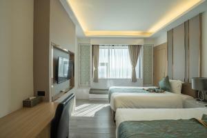 ein Hotelzimmer mit zwei Betten und einem Flachbildfernseher in der Unterkunft Enrich Grand Hotel in Bangkok