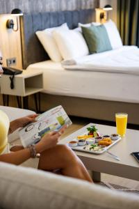 een vrouw zit op een stoel een boek te lezen en eet een bord vol eten bij Ayçiçeği Comfort Otel in Edirne