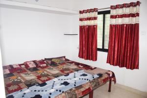 a bedroom with a bed and two windows with red curtains at Daneshwari Bhakt Niwas in Akalkot