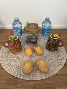 ein Teller mit Croissants, zwei Tassen und Wasserflaschen in der Unterkunft Chez Carla in Sisteron