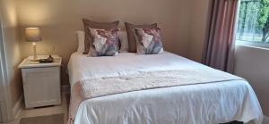 a bedroom with a white bed with pillows and a window at Flanders South Cottage in Gqeberha