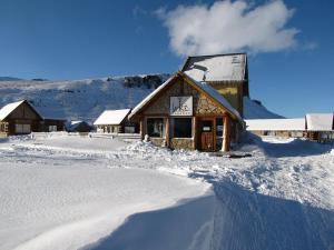 een gebouw bedekt met sneeuw met een berg op de achtergrond bij Cabañas Aike in Caviahue