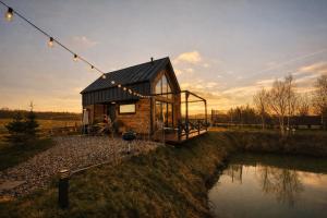 ein winziges Haus mit schwarzem Dach neben einem Fluss in der Unterkunft Hulaj Dusza - dom nad stawem 