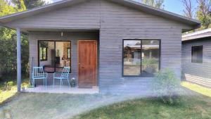 ein kleines graues Häuschen mit einer Tür und zwei Stühlen in der Unterkunft Cabañas en la naturaleza in Villarrica