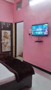 a room with a pink wall with a flat screen tv at Shikhar guest house 1 in Ujjain