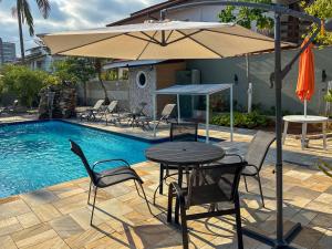 a table and chairs with an umbrella next to a pool at Moreno Guest House com Piscina, churrasqueira Praia de Itaguaré e Riviera in Bertioga +50 photos