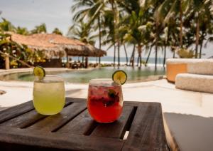two cocktails sitting on a wooden table next to a pool at Puertas Paraíso Hotel boutique in Zihuatanejo
