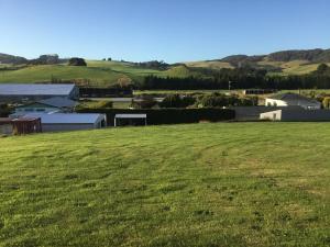 a field of green grass with buildings in the background at South Catlins Cottage in Tokanui