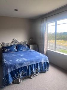 een slaapkamer met een blauw bed en een groot raam bij Sunny garden view suite with private bathroom in Auckland