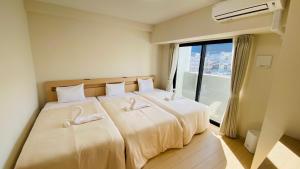 een slaapkamer met twee bedden met witte lakens en een raam bij Apartment Hotel YAEZAKI in Wada