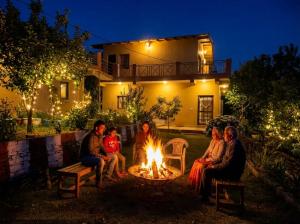 eine Gruppe von Menschen, die vor einem Haus um ein Feuer sitzen in der Unterkunft Rooptara Valley Luxury Cottage Majkhali Himalaya in Rānīkhet