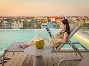 une femme assise sur une chaise en lisant un livre à côté d'une piscine dans l'établissement 酒店MARQUIS HOTEl, à Ban Bang Toei (1)