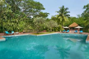 a swimming pool at a resort with blue chairs and trees at Blue Ocean The Fern Resort & Spa Ganpatipule, Series by Marriott in Ganpatipule