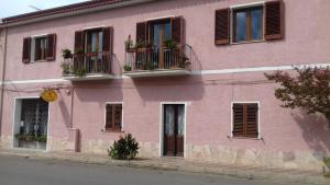 un bâtiment rose avec des fenêtres et des plantes. dans l'établissement Canne Al Vento, à Teulada