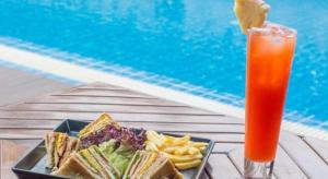 ein Teller mit Sandwiches und Chips und ein Getränk neben einem Pool in der Unterkunft PhoomThai Garden Hotel in Phrae