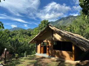 a small building with a roof with mountains in the background at Pepper Hills Hostel & Cottages in Ella